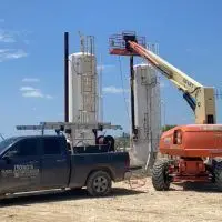 Long's Pest Control truck beside a boom lift at an oilfield tank site