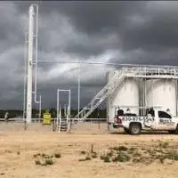 Long's Pest Control truck at an oilfield tank battery under storm clouds