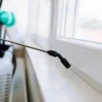 A person is spraying a window sill with a sprayer.